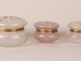 three small glass jars with gold trims and lids on a white surface
