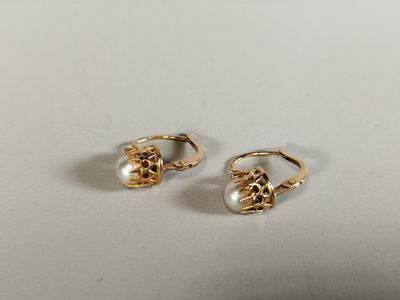 une paire de boucles d'oreilles en or et perles posées sur une surface blanche