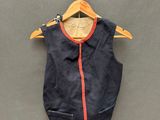 gilet bleu marine avec des bordures orange, suspendu à un cintre sur un mur gris