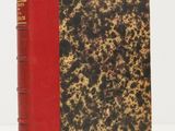 un vieux livre posé sur une table blanche à côté d'un livre rouge
