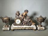 une statue représentant une femme assise sur une table, à côté de trois vases et d'une horloge