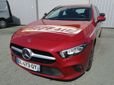 La Mercedes CLA est garée devant un immeuble sur lequel est accrochée une pancarte « À vendre ».