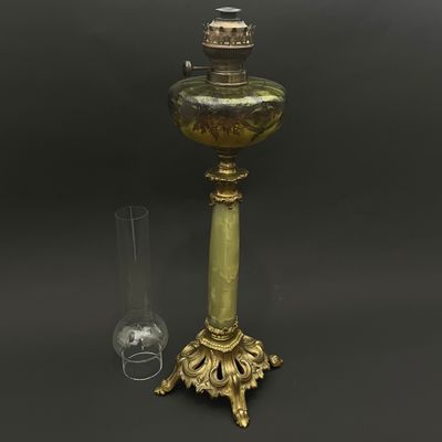 une image représentant une lampe de couleur dorée, dotée d'un abat-jour en verre, posée sur une table