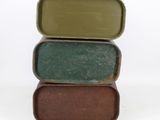 three tins of soap sitting on top of each other on a white surface