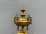 un vase doré posé sur un socle, sur fond gris