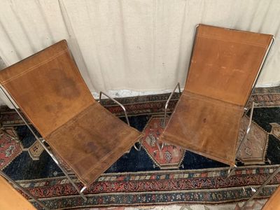 une paire de fauteuils en cuir posés sur un tapis devant un rideau blanc