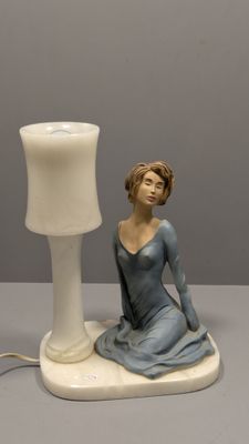 une figurine représentant une femme assise sur une table, à côté d'une lampe