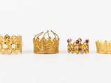 four gold crown rings and a ring with diamonds on a white surface