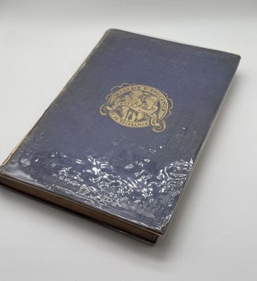 an old book sitting on a white table with a gold emblem on it
