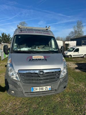 une photo montrant une camionnette argentée garée dans un champ, avec d'autres véhicules en arrière-plan