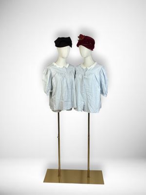 two mannequins dressed in blue shirts and red hats stand on a gold stand