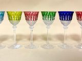 six verres à vin colorés alignés en rang sur une surface blanche