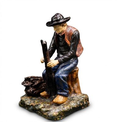 figurine of a man sitting on a tree stump with a rifle