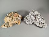 two pieces of rock with white and black crystals on a gray surface