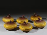 six bols jaunes et marron avec leurs couvercles, posés sur une surface blanche