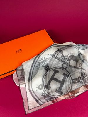 an orange box with a white scarf and a black and white scarf on a pink surface