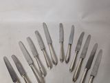 six silverplated knives are arranged in a circle on a white surface