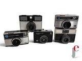 several old cameras are lined up in a row on a white surface