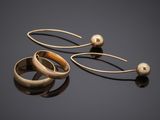 two gold rings and a pair of earrings on a black surface
