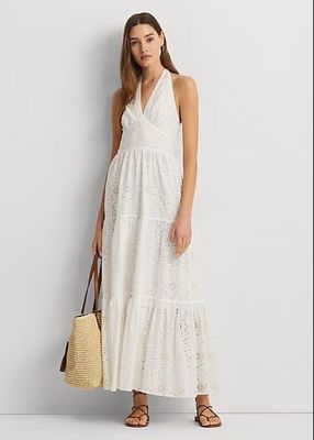 Une femme vêtue d'une robe blanche et de sandales se tient adossée à un mur.