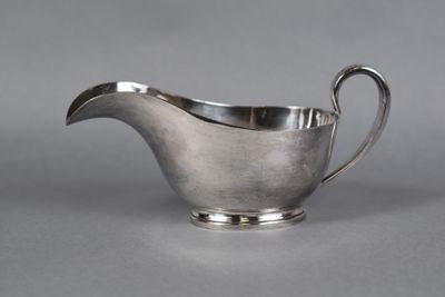 a silver sauce boat with a curved handle on a gray surface