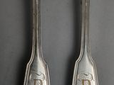 two silver spoons with initials on them sitting on top of a table