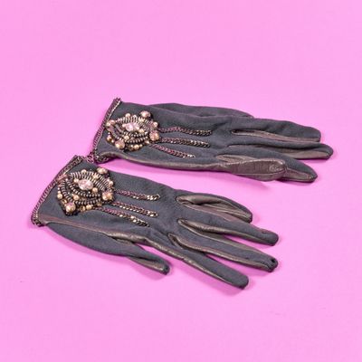 une paire de gants en cuir noir ornés de perles sur fond rose