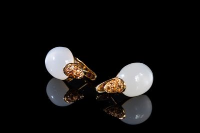 une paire de boucles d'oreilles blanches et dorées posées sur un fond noir