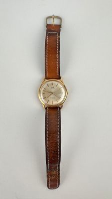 gros plan d'une montre sur une surface blanche avec un bracelet marron