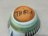 a green and white vase with a brown label on it