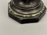 une statue en bronze représentant un homme, posée sur un socle posé sur une table