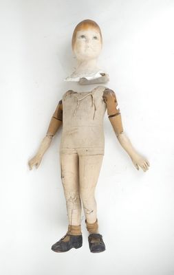une vieille poupée en bois vêtue d'une chemise blanche et d'un pantalon marron