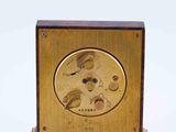 a gold clock on a wooden stand on a white surface