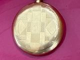 a gold pocket watch on a pink surface