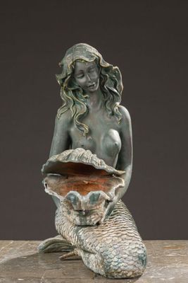a statue of a mermaid sitting on a rock holding a shell