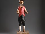 statue of a man in a red vest and hat standing on a wooden block