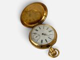 une montre de poche en or avec un cadran blanc sur une surface blanche