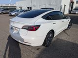 the back of a white car parked in a parking lot next to a building