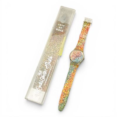 une image représentant une montre et une boîte de paillettes posées sur une surface blanche