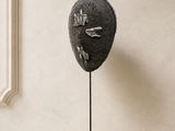 une sculpture représentant un visage, posée sur un socle devant une fenêtre
