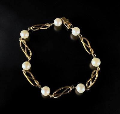 a gold bracelet with pearls on a black background