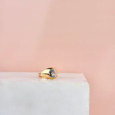 une bague en or sertie d'une topaze bleue repose sur un bloc blanc