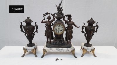 trois statues posées sur une table, avec une horloge au milieu