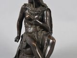 bronze statue of a woman sitting on a rock with her hands on her knees