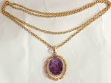 a gold necklace with a purple stone on a white background