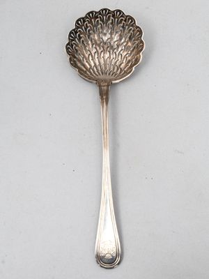 une cuillère ancienne en argent posée sur une surface blanche, avec un manche en argent