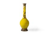 un vase jaune posé sur une surface blanche, sur fond blanc