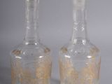 deux bouteilles en verre transparent ornées de motifs dorés, posées l'une à côté de l'autre