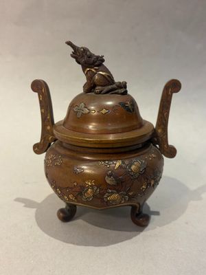 une image représentant un petit pot en bronze surmonté d'un oiseau