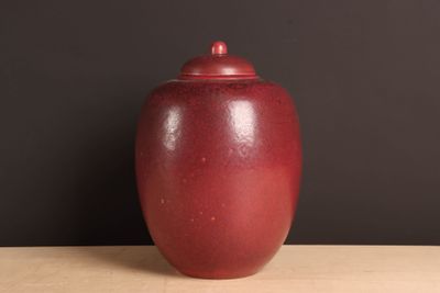 un vase rouge posé sur une table, avec un mur noir en arrière-plan